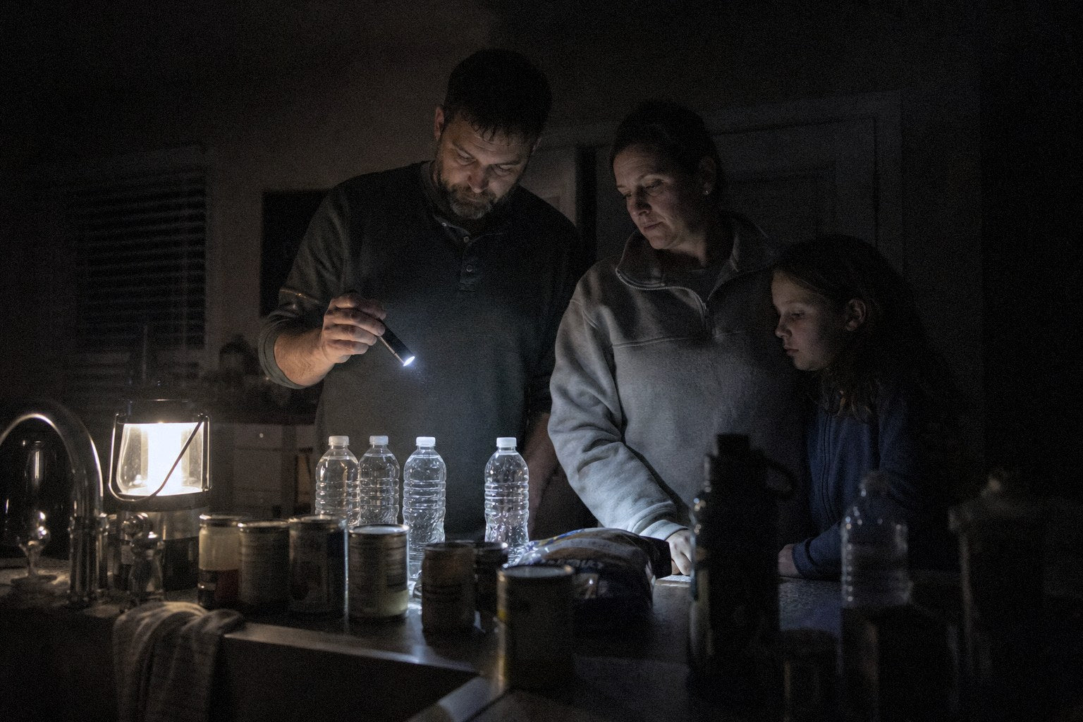 A family in a dark kitchen during a power outage, checking supplies by lantern light